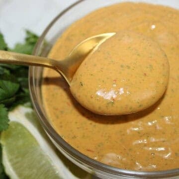 Close-up of chipotle mayo sauce in a glass bowl with herbs and lime.