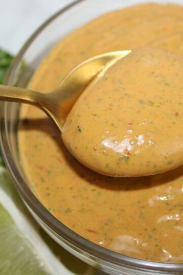 Close-up of chipotle mayo sauce in a glass bowl with herbs and lime.