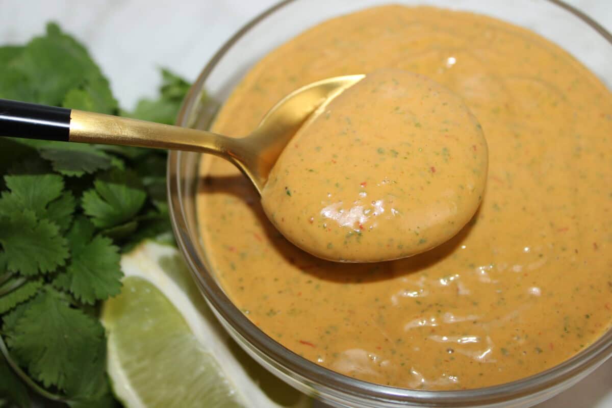 Close-up of chipotle mayo sauce in a glass bowl with herbs and lime.